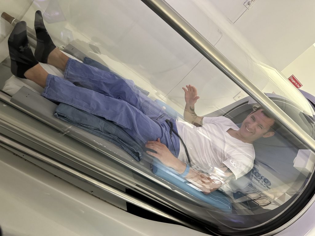Jeff waving from inside a hyperbaric oxygen therapy chamber during treatment.